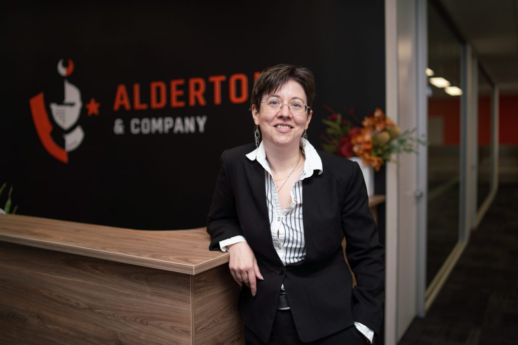 Lucy Oborn leaning on a reception counter with the Alderton & Company logo in the background.